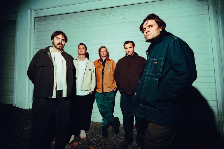 New Zealand indie band No Cigar members posing together at night in front of a closed garage door in a promo photo by Tom Grut.